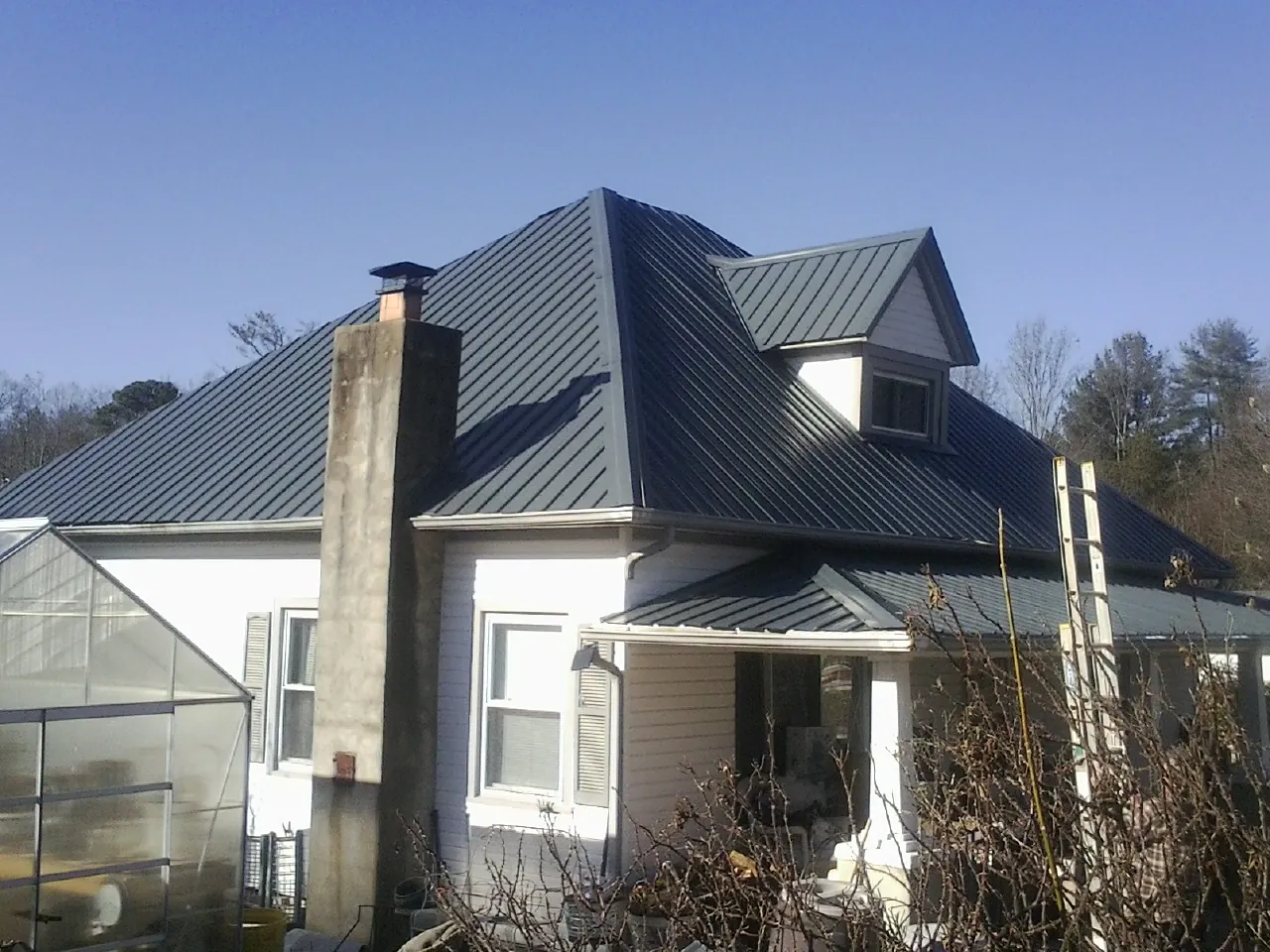 Dark blue standing seam metal roof on a white farmhouse with dormer — Slate & Tile Roof Repair by Roofing Brothers in Patton