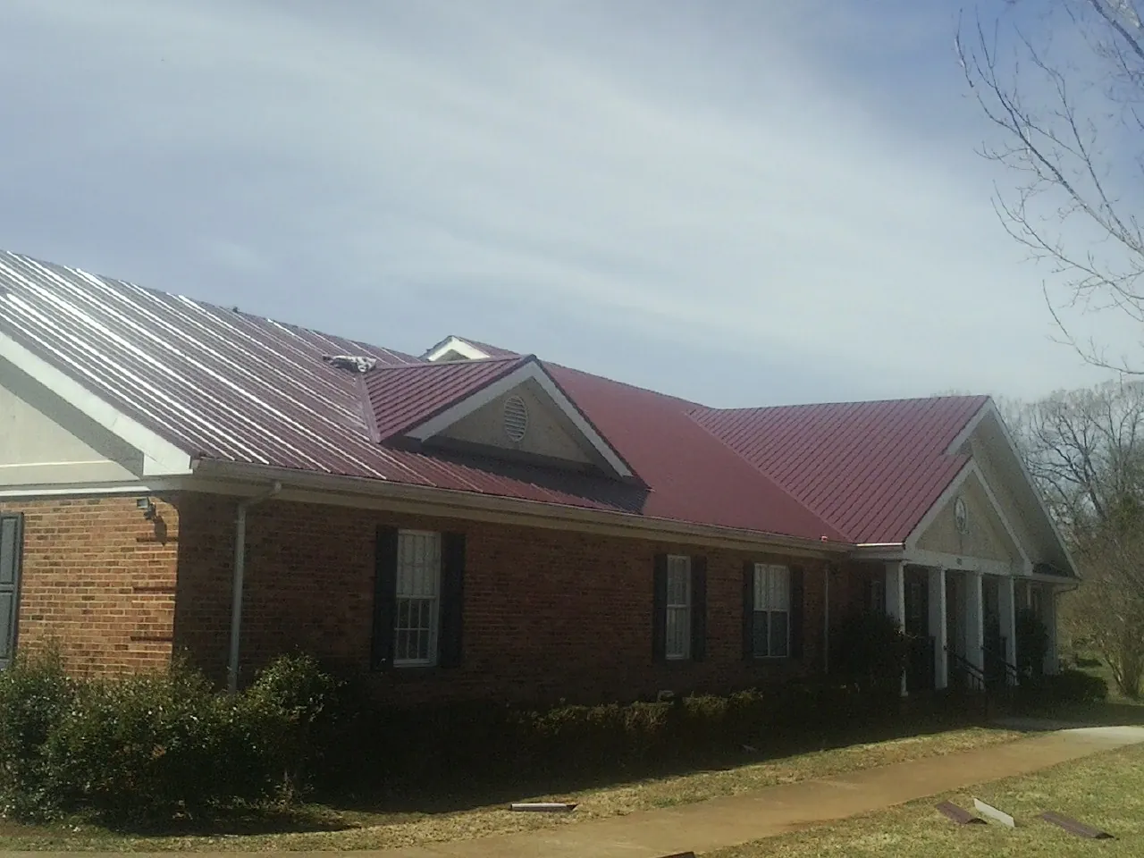 Red metal roof with gabled entries on a long brick building, from a Hail Damage Roof Repair job in Patton