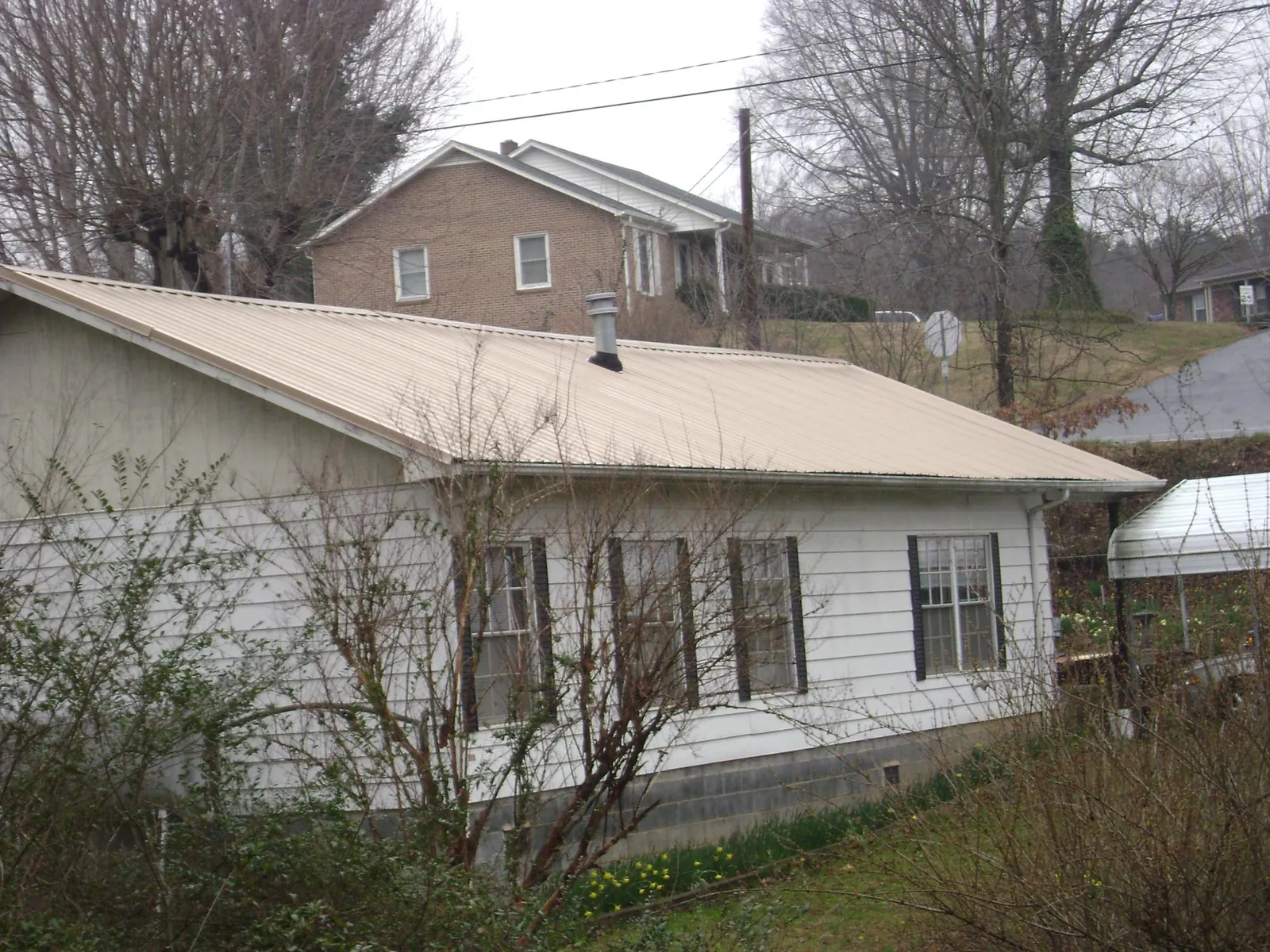 Tan metal roof on a white sided house set into a hillside — Commercial Roofing by Roofing Brothers in Patton